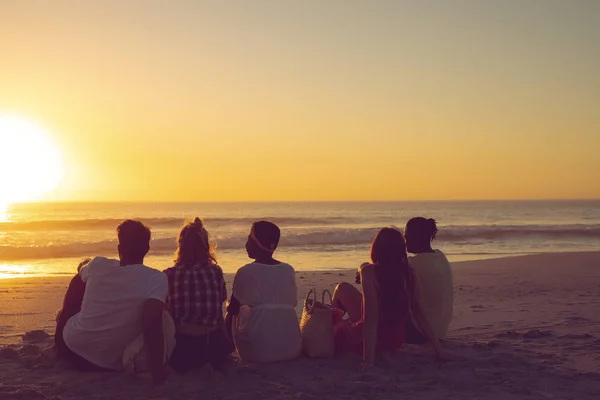 Vista Trasera Diversos Amigos Sentados Juntos Playa Durante Atardecer —  Fotos de Stock
