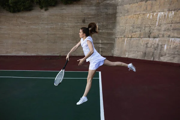 一个年轻的白人女子打网球 还球和跳墙的侧视图 — 图库照片