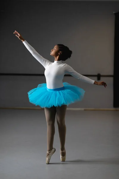 一个混血的女芭蕾舞演员头戴白色的三分球和蓝色的燕尾服 在一个明亮的演播室里跳舞 胳膊抬起来的镜头 — 图库照片