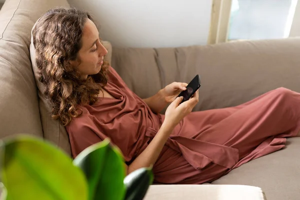 Белая женщина проводит время дома, используя свой смартфон. Стиль жизни дома изолирует, социальное дистанцирование в карантинной изоляции во время пандемии коронавируса ковид 19. — стоковое фото