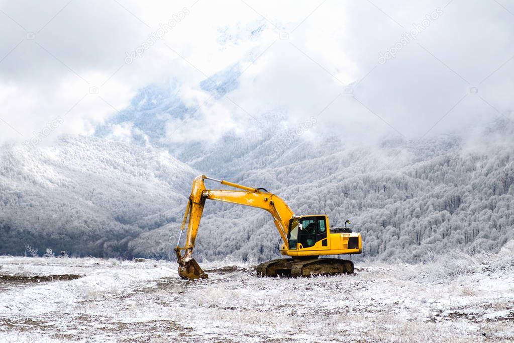Yellow excavator on a background of snowy mountains