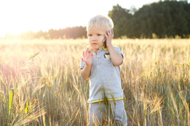 Çok güzel çocuk çavdar batan güneşin ışınları içinde dolu bir alanda bir cep telefonunda konuşuyor
