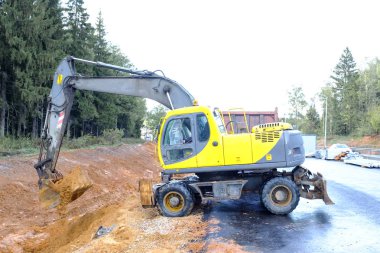 Sarı bir tekerlekli ekskavatör Kazı çalışmaları gerçekleştirir. Kazılar zemin toprak bir kova ile.