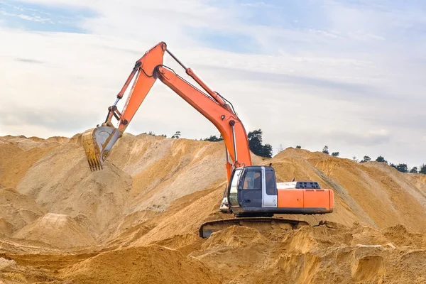 Escavadora de esteiras trabalha em um canteiro de obras. Equipamento de construção pesado em um contexto de montanhas de areia. Uma máquina goteja areia com um balde . — Fotografia de Stock