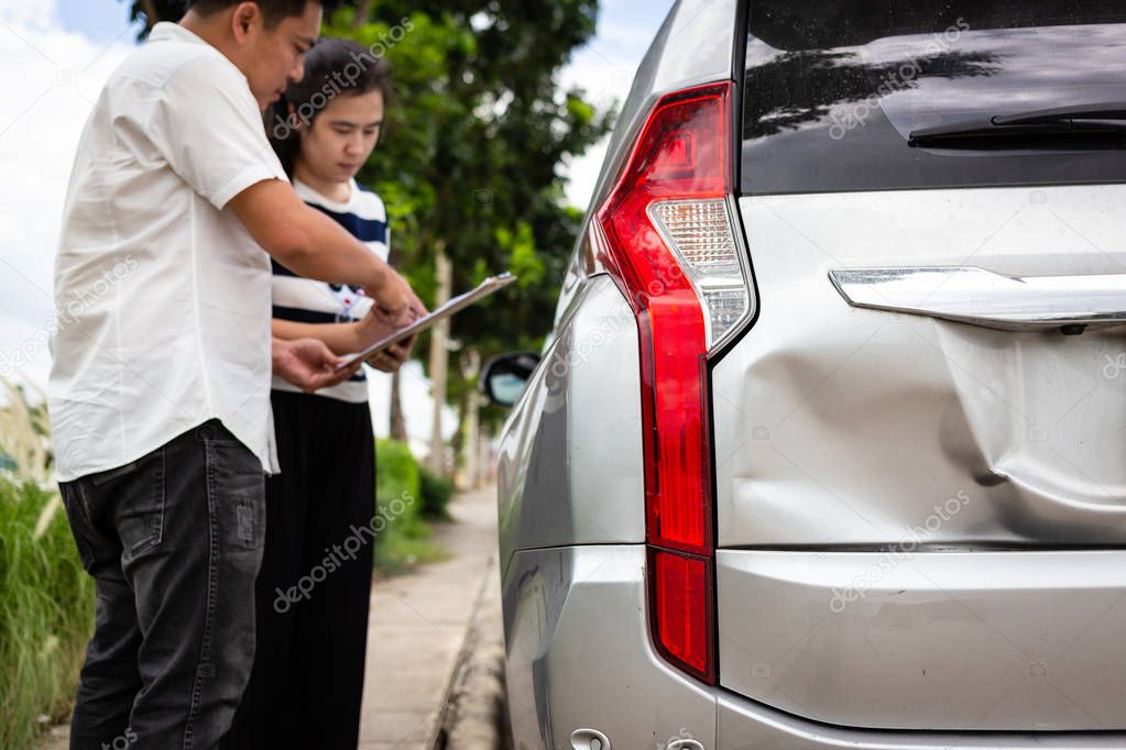 Insurance agent writing on clipboard while examining the car after accident claim was assessed and processed,traffic accident and insurance concept