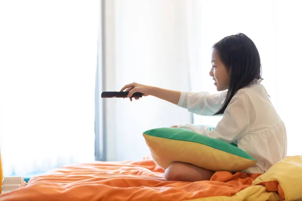 亚洲女孩看电视躺在床上与遥控在手 — 图库照片