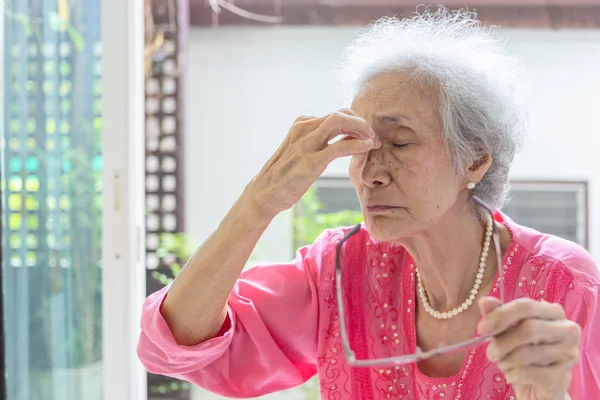 Asiatische ältere Frau, die Nasenbrücke massiert, Augenüberlastung oder Kopfschmerzen spürt und eine Brille hält, die an Augenkrankheit, Augenermüdung, medizinischem und medizinischem Konzept leidet — Stockfoto