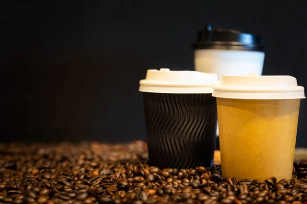 Cardboard coffee cup,disposable plastic and paper cup,brown,black,white paper coffee cup and roasted coffee beans on black background for hot drinks,coffee take away package at cafe shop