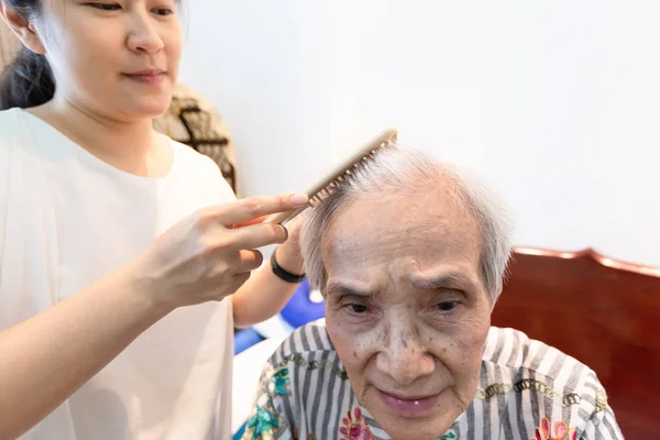 Азиатская молодая женщина расчесывание волос пожилой женщины в доме, уход помощник расчесывания волос пожилой женщины пациент в доме престарелых, концепция ухода за пожилыми людьми — стоковое фото