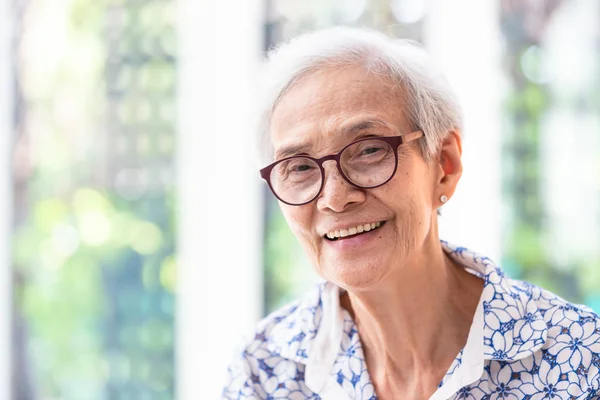 Primer plano asiático anciana mujer en gafas mostrando saludable recta dientes, retrato senior mujer sonriendo sintiéndose feliz, hermosa hembra mirando a cámara en casa —  Fotos de Stock