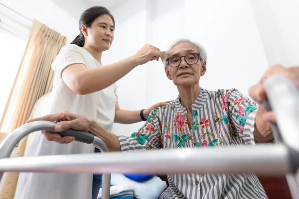 Asyalı genç kadın ya da bakım asistanı evde walker ile yaşlı kadının saç tarama, torunu yatay görünümü büyükanne saç tarama, kavram yaşlı bakımı — Stok fotoğraf