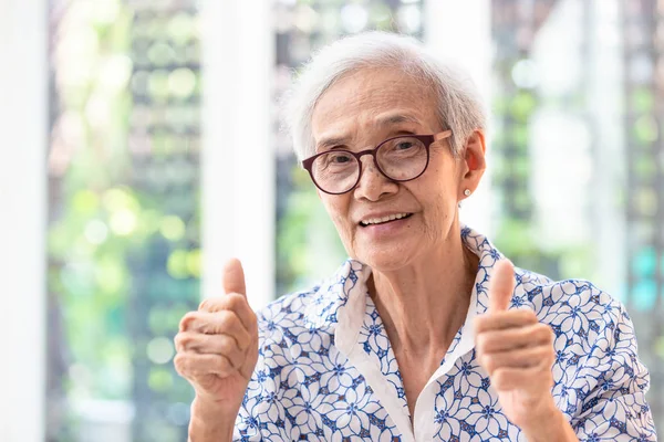 Asiatique femme âgée dans des lunettes, montrant pouces satisfaits du service, souriant femme âgée montrer pouce geste — Photo
