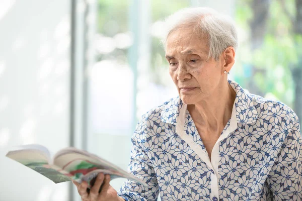 집에서 편안한 책을 읽는 아시아 노인 여성,노인 여성은 책을 읽는 자유 시간을 보낸다. — 스톡 사진
