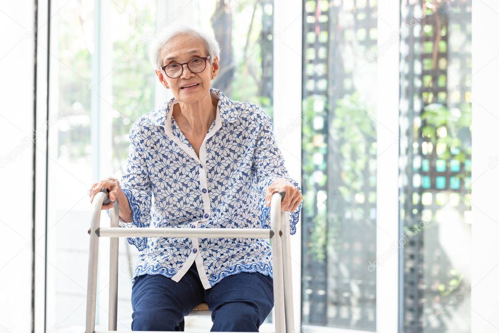 Asian senior woman sitting with walker during rehabilitation, elderly woman wear glasses,smiling and looking at camera in home