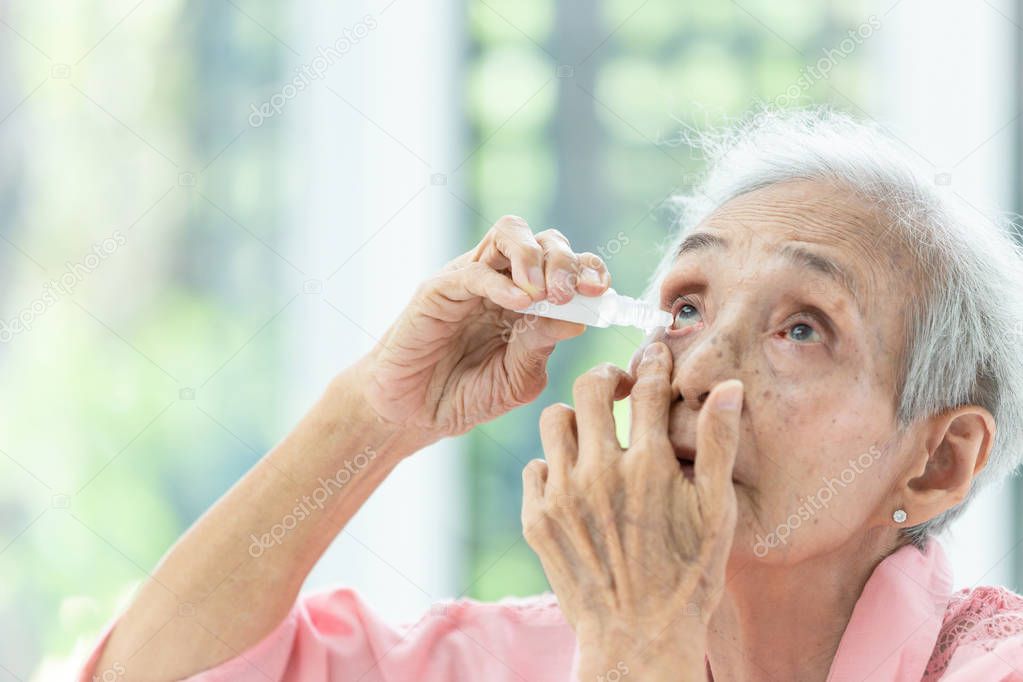 Asian senior woman putting eye drop,closeup view of elderly person using bottle of eyedrops in her eyes,sick old woman suffering from irritated eye,optical symptoms,health concept
