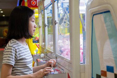 Pençe oyun veya kabine oynayan Asya küçük kız alışveriş merkezi Outlet birinde bebek yakalar, alışveriş merkezi merkezinde bilgisayar makineleri sevimli çocuk oyun arcade oyunları tatil etkinlikleri, tatil konsepti