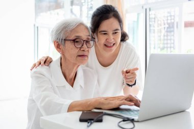 Mutlu kıdemli anne ve onun yetişkin kızı online alışveriş yaparken, evde masada dizüstü bilgisayar ile internette sörf, asya yaşlı kadın bilgisayar ve serf web siteleri önünde oturup, teknoloji ve eğitim kavramı