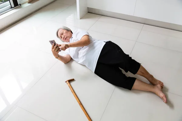 Asiatiska äldre människor med käpp och använda telefonen för att ringa efter hjälp, sjuk Senior Kvinna med huvudvärk, ryggvärk liggande på golvet efter att falla ner, lider av sjukdom, yrsel, svimma och ringer via telefon till nödsituation — Stockfoto