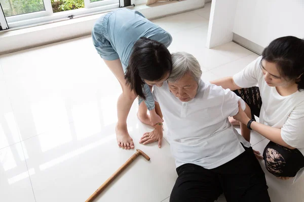 Asiatiska äldre människor med käpp på golvet efter att falla ner och omtänksam ung kvinna assistent, sjuk Senior kvinna eller mor föll till golvet på grund av yrsel, svimma, lider av sjukdom och med en dotter, barnbarn att hjälpa henne — Stockfoto