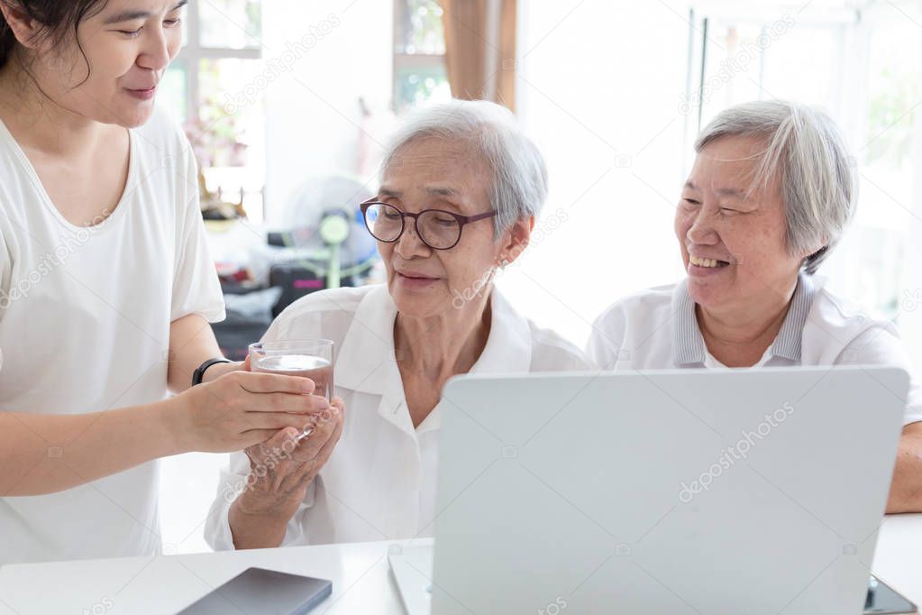 Daughter giving or serving cups of water for mother to drink,,Happy two senior asian woman,sisters or friends talking with laptop computer together at home,smiling elderly people and her friendship,concept friend and family