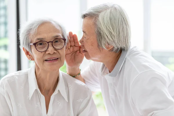 アジアの先輩女性が口の近くでおかしいと言い、友人に耳を傾け、高齢の女性の耳と顔の近くで話し、聞こえにくい、聴覚障害、聴覚障害、聴覚障害を持つ高齢者 — ストック写真