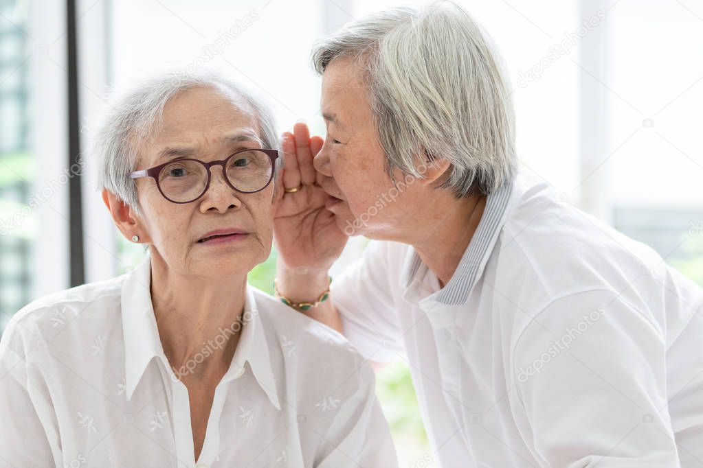 Asian senior woman holding hand near mouth telling funny,gossips  on ears to friend,speaking in elderly woman ear and near face,having difficulty in hearing,hard to hear,hearing impairment,hearing impaired old people