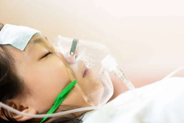 Asian little girl with oxygen mask and cold gel placed on her forehead to relief fever,cute child patient putting inhalation in hospital bed or home,intensive care,health care,support,help concept