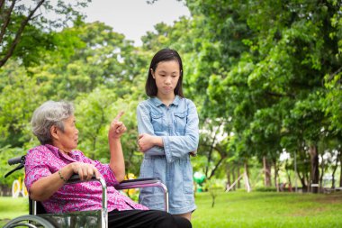 Tekerlekli sandalyede Asyalı yaşlı kadın kızgın, işaret parmağını, açık parkta küçük çocuk kız admonishing, büyükanne duygu ifade duygu, uyarı, kötü davranış için itaatsiz torunu azarlama