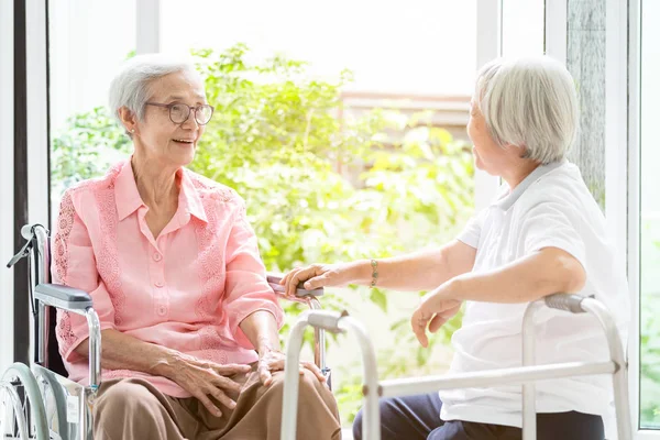 Fröhliche asiatische Seniorin im Rollstuhl, Schwester oder Freundin mit Rollator, die Spaß hat, freundliche, weibliche ältere Menschen lächeln und ihre Freundschaft spricht, lacht zu Hause, Familie, Rentenkonzept — Stockfoto