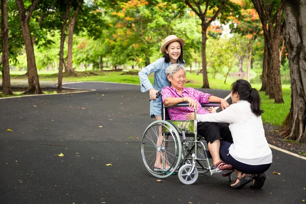 Азіатський старший жінка в інвалідному візку з маленькою дитиною дівчата підтримки, насолоджуватися на ходьбі зеленої природи, бабусі зі своєю донькою, внучка весело говорити, обійняти, сміятися разом у літній відкритий парк, літнім догляд, сімейна концепція — стокове фото
