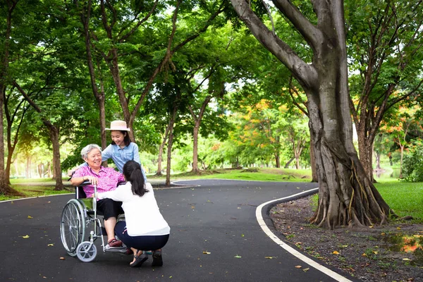 Asian senior woman having happiness,smiling with her daughter  and granddaughter on wheelchair at outdoor park,elderly woman is happy with their family,child girl having fun talk,hug,laughing together,happy family concept