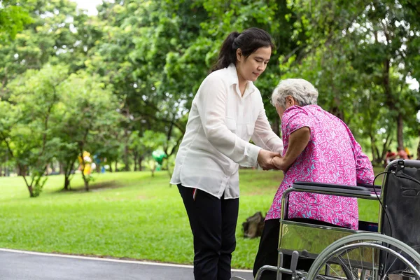 Kadın caregiver Asya ya da genç hemşire desteği, açık park tekerlekli sandalyeye ayakta durmak için kıdemli kadın yardım, yaz aylarında kızı ile hasta anne yeşil doğa, Aile, yaşlı bakım kavramı — Stok fotoğraf