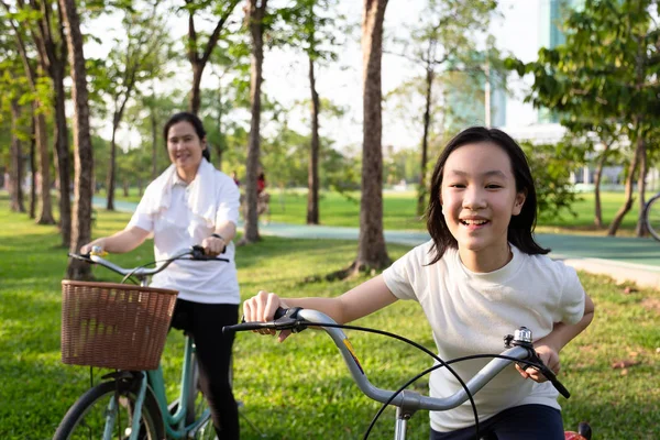Happy asian little girl child with bicycle in outdoor park, smiling daughter with mother on a bike ride together, family activities on weekend — стоковое фото