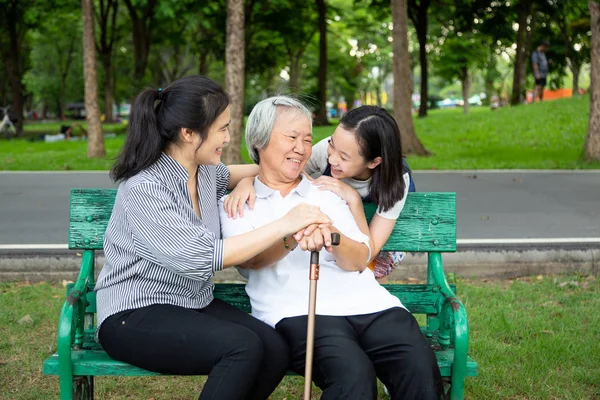 Glückliche asiatische Familie im Outdoor-Park, lächelnde Seniorin, die auf einer Bank sitzt, während ihre Tochter und Enkelin sie umarmen, Großmutter mit Rollator in der Hand, Familien-, Sommer- und Altenpflegekonzept — Stockfoto