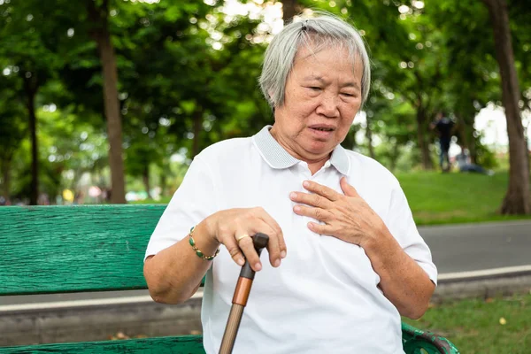 Asiatische ältere Menschen mit bestimmten Symptomen, Atembeschwerden, Leiden oder Herzproblemen, kommuniziert die Symptome von Herzkrankheiten, ältere Frau mit Brustschmerzen, die an Herzinfarkt im Outdoor-Park leidet, Gesundheitswesen und medizinisches Konzept — Stockfoto