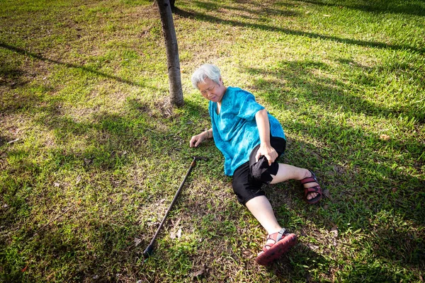 亚洲老人在夏天户外公园摔倒后，手杖掉在地上，生病的老年妇女因头晕、昏厥或意外，生病、腿部、膝盖疼痛或骨痛而倒在地上 — 图库照片
