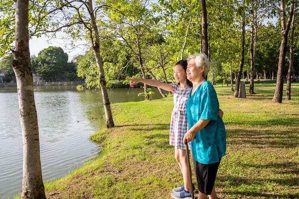 Malá Asijská holčička, která podporuje starší ženu s chodící holí, šťastná usměvavá babička a vnučka ve venkovním parku, starší lidé chodí cvičit pro zdraví, rodinu konceptů; léto a prázdniny — Stock fotografie
