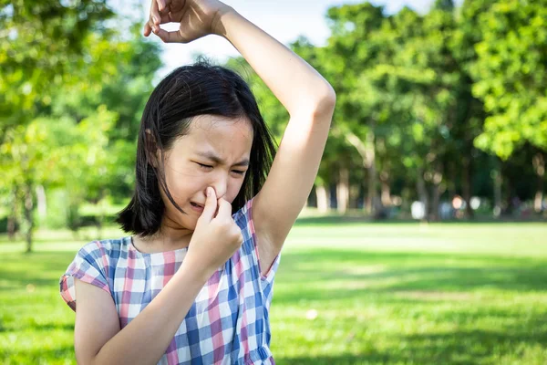 Closeup asian cute little girl feel bad foul odor situation,smelling,sniffing her wet armpit in outdoor park,beautiful child feeling smell of sweat, problems due to hormonal changes,motion facial expression reaction