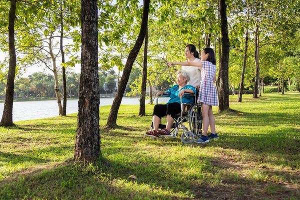 Asian senior woman or mother with her daughter and smiling of  child girl or granddaughter watching something interesting together in summer outdoor park,elderly people in wheelchair with their family,happy family,vacation concept