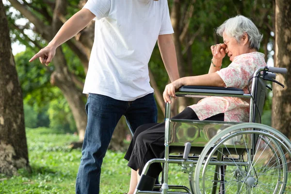 Malheureux, problèmes famille asiatique, homme en colère ou soignant masculin expulsé sa femme âgée en fauteuil roulant querelle, dispute, mère aînée pleurer en plein air, fils agressif, famille, violence, concept ingrat — Photo