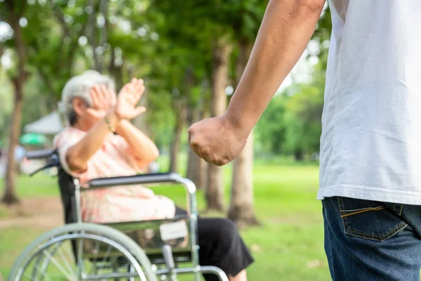 Asian elderly woman in wheelchair were physically abused,attacking in outdoor,stop physical abuse senior people,angry man or caregiver raised punishment fist,stop violence and aggression concept — Stock Photo, Image