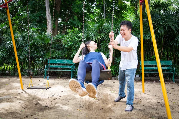 Happy asian little child girl having fun, enjoy, playful, playing on the swing, beautiful daughter riding on swing in the playground, smile father pushing, dad swinging her in outdoor park, holiday family concept — Stock fotografie