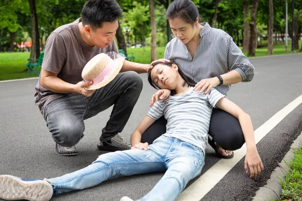 Asian little child with heat stroke,high temperature, vertigo,dizziness,sick daughter on a sunny day,cute girl having exhausted suffering from sunburn very hot in summer outdoor, feeling faint,father and mother assisting,help,care her — Stock Photo, Image