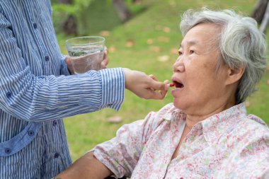 Asyalı kız çocuğu ya da bakıcı ilaç hapları ya da el ya da parmak ve su kapsülleri, yaşlı anneye hap vermek, hasta yaşlı bir kadın, vitamin, antibiyotik, ağrı kesici, tekerlekli sandalye parkında besin takviyeleri, sağlık hizmetleri