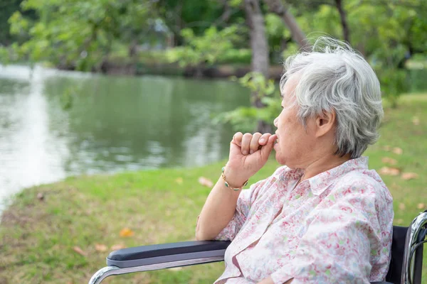 亚裔老妇人感到压力大，担心女性在轮椅户外公园咬指甲，老人有紧张表情，指甲咬，急着用手咬指甲，焦虑问题 — 图库照片