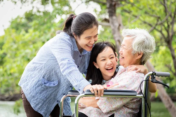 Familia asiática, abuela mayor, madre, hija sonriente disfrutar, abrazos en el parque al aire libre, ancianos pacientes riendo hablar divertido con la familia en silla de ruedas, mujer feliz y cuidado de niña pequeña con ella, amor, relación, concepto de cuidado de la salud — Foto de Stock