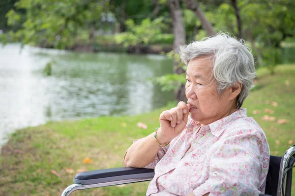 亚裔老妇人感到压力大，担心女性在轮椅户外公园咬指甲，老人有紧张表情，指甲咬，急着用手咬指甲，焦虑问题 — 图库照片