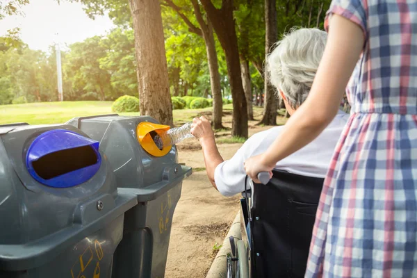 Asian senior woman hand holding plastic bottle,putting plastic water bottle in recycling bin,elderly tourist hand throwing garbage in a trash bin on street in outdoor park,environmental protection,global warming concept — 스톡 사진