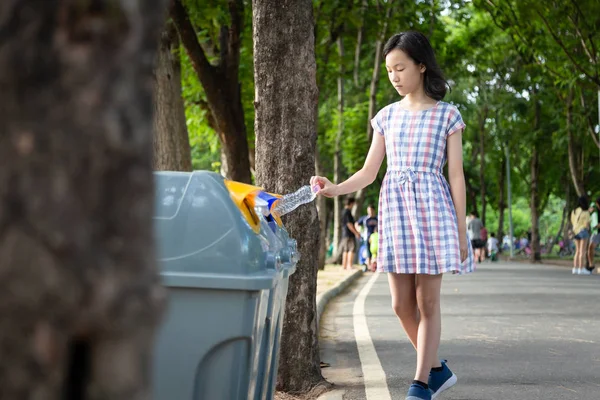 Asiatico bambina mano tenendo bottiglia di plastica, mettendo bottiglia d'acqua di plastica nel cestino di riciclaggio, donna turistica mano gettando spazzatura in un cestino sulla strada nel parco all'aperto, protezione dell'ambiente, concetto di riscaldamento globale — Foto Stock