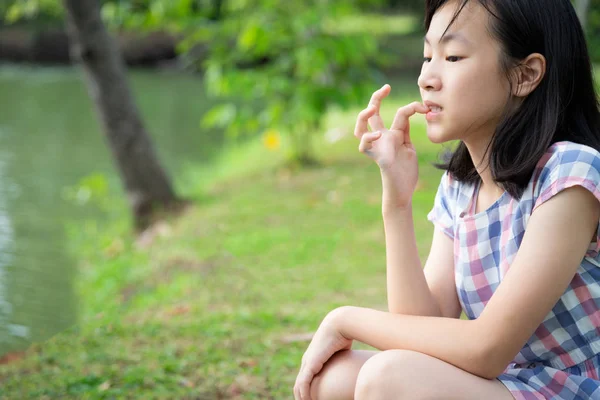 Asian little child girl feeling stressed,female worried bites  finger nails in outdoor park,girl patient with nervous expression,nail biting,anxious with hand on mouth biting her nails,anxiety problem,mental health
